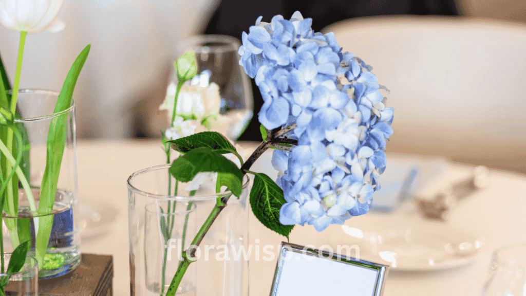 Elegant blue hydrangea centrepieces arranged with white roses and greenery, perfect for weddings, events, or home décor.

